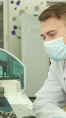 Üst düzey bir laboratuvarda odaklanmış beyaz önlük ve koruyucu maske takmış genç bir laboratuvar asistanı modern bilgisayarında test sonuçlarını dikkatle inceliyor. Eldivenli elleri klavyede zarifçe geziniyor, özünü somutlaştırıyor.