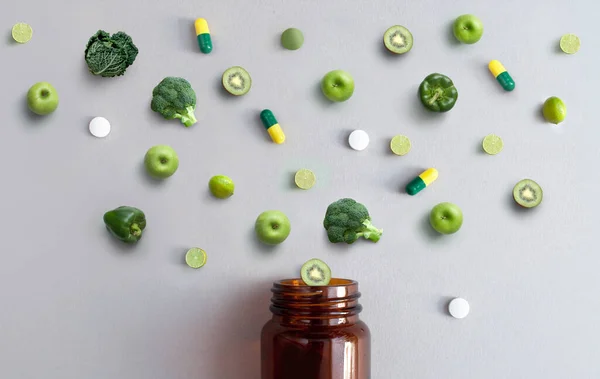 リンゴ ブロッコリー キャベツ ライム キウイと一緒に緑のビタミン薬とカプセル薬瓶から出てくる 栄養抗酸化概念 — ストック写真
