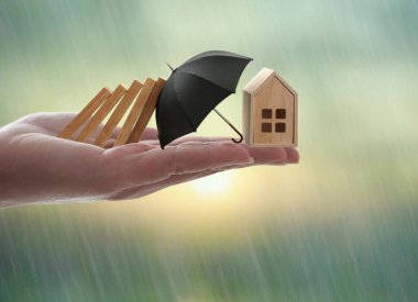 El ele tutuşan dominolar minyatür evin üzerine düşmesini engelliyor, ev sigortası konsepti, pencereden görülebilen yağmur.