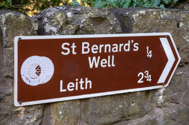 Edinburgh, Scotland - February 17th 2023: A signpost on a wall on the Water of Leith, marking the distance to St. Bernards Well and Leith in Edinburgh, Scotland. clipart