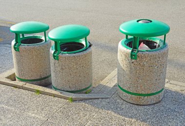 Yeşil yuvarlak metal kapaklı üç beton çöp bidonu