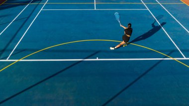 Yepyeni bir kortta genç bir bayan tenisçinin kuş bakışı görüntüsü. Bu fotoğraf, oyuna benzersiz bir bakış açısı kazandırmak için bir drone ile çekildi.. 