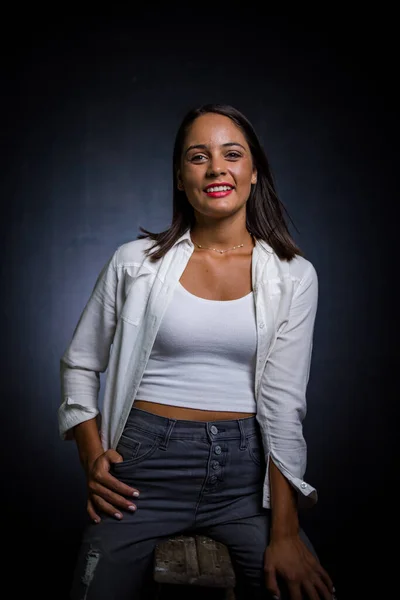 Pretty dark haired girl posing for a fashion shoot in a studio. She is dressed in stylish jeans and a crop top, and her poses convey a sense of youthfulness and vitality.