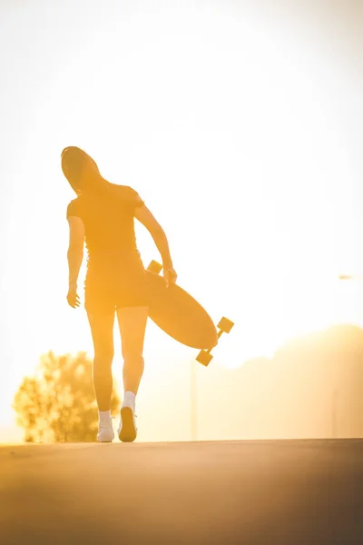 活気のある都市環境で暗い髪のスケートボードを持つかなり若い女性 — ストック写真