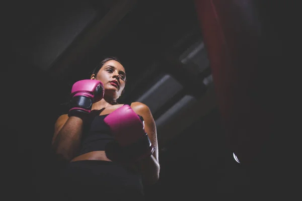 一个黑头发的女孩在黑暗和情绪低落的环境下打了一袋拳 她戴着拳击手套 全神贯注于训练或日常锻炼 — 图库照片