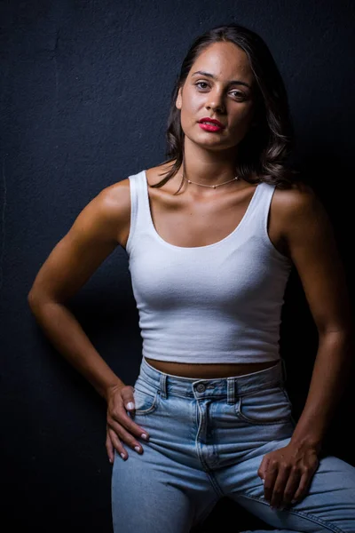 Pretty dark haired girl posing for a fashion shoot in a studio. She is dressed in stylish jeans and a crop top, and her poses convey a sense of youthfulness and vitality.