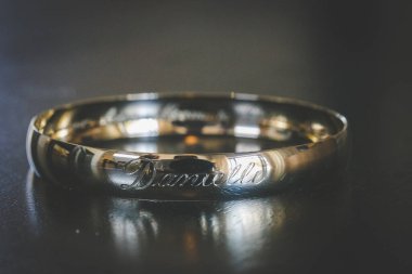 Nikah yüzüklerinin bu çarpıcı yakın plan görüntüsü, sevgi dolu düğün geleneğinin güzelliğini ve sembolizmini yansıtıyor. Fotoğrafta gelinin ve damadın alyansları tarafsız bir zemine yerleştirilmiş. Karmaşık detayları vurguluyor.