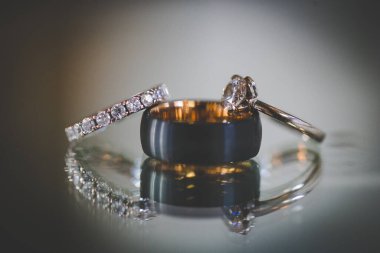 Nikah yüzüklerinin bu çarpıcı yakın plan görüntüsü, sevgi dolu düğün geleneğinin güzelliğini ve sembolizmini yansıtıyor. Fotoğrafta gelinin ve damadın alyansları tarafsız bir zemine yerleştirilmiş. Karmaşık detayları vurguluyor.
