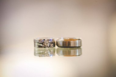 Nikah yüzüklerinin bu çarpıcı yakın plan görüntüsü, sevgi dolu düğün geleneğinin güzelliğini ve sembolizmini yansıtıyor. Fotoğrafta gelinin ve damadın alyansları tarafsız bir zemine yerleştirilmiş. Karmaşık detayları vurguluyor.