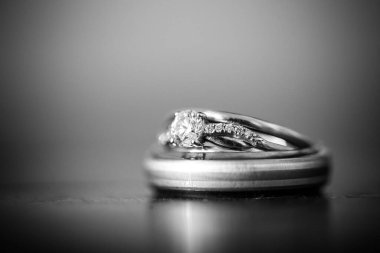 Nikah yüzüklerinin bu çarpıcı yakın plan görüntüsü, sevgi dolu düğün geleneğinin güzelliğini ve sembolizmini yansıtıyor. Fotoğrafta gelinin ve damadın alyansları tarafsız bir zemine yerleştirilmiş. Karmaşık detayları vurguluyor.
