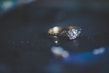 Nikah yüzüklerinin bu çarpıcı yakın plan görüntüsü, sevgi dolu düğün geleneğinin güzelliğini ve sembolizmini yansıtıyor. Fotoğrafta gelinin ve damadın alyansları tarafsız bir zemine yerleştirilmiş. Karmaşık detayları vurguluyor.