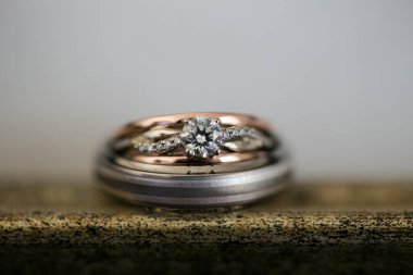 Nikah yüzüklerinin bu çarpıcı yakın plan görüntüsü, sevgi dolu düğün geleneğinin güzelliğini ve sembolizmini yansıtıyor. Fotoğrafta gelinin ve damadın alyansları tarafsız bir zemine yerleştirilmiş. Karmaşık detayları vurguluyor.