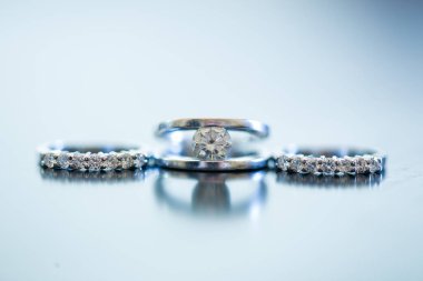 Nikah yüzüklerinin bu çarpıcı yakın plan görüntüsü, sevgi dolu düğün geleneğinin güzelliğini ve sembolizmini yansıtıyor. Fotoğrafta gelinin ve damadın alyansları tarafsız bir zemine yerleştirilmiş. Karmaşık detayları vurguluyor.