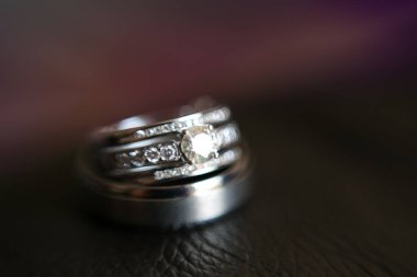Nikah yüzüklerinin bu çarpıcı yakın plan görüntüsü, sevgi dolu düğün geleneğinin güzelliğini ve sembolizmini yansıtıyor. Fotoğrafta gelinin ve damadın alyansları tarafsız bir zemine yerleştirilmiş. Karmaşık detayları vurguluyor.