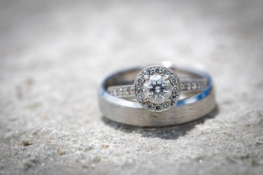 Nikah yüzüklerinin bu çarpıcı yakın plan görüntüsü, sevgi dolu düğün geleneğinin güzelliğini ve sembolizmini yansıtıyor. Fotoğrafta gelinin ve damadın alyansları tarafsız bir zemine yerleştirilmiş. Karmaşık detayları vurguluyor.