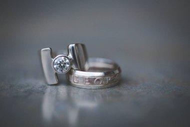Nikah yüzüklerinin bu çarpıcı yakın plan görüntüsü, sevgi dolu düğün geleneğinin güzelliğini ve sembolizmini yansıtıyor. Fotoğrafta gelinin ve damadın alyansları tarafsız bir zemine yerleştirilmiş. Karmaşık detayları vurguluyor.