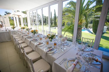 Bu büyüleyici görüntü, gerçek bir düğünün zarif dekorunu ve büyüleyici çiçek düzenlemelerini gözler önüne seriyor. Fotoğrafta zarif çiçekler, mumlar ve diğer dekoratif el ile süslenmiş büyüleyici bir düğün yerinde güzel dekore edilmiş bir masa yer alıyor.