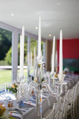 Bu büyüleyici görüntü, gerçek bir düğünün zarif dekorunu ve büyüleyici çiçek düzenlemelerini gözler önüne seriyor. Fotoğrafta zarif çiçekler, mumlar ve diğer dekoratif el ile süslenmiş büyüleyici bir düğün yerinde güzel dekore edilmiş bir masa yer alıyor.