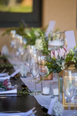 Bu büyüleyici görüntü, gerçek bir düğünün zarif dekorunu ve büyüleyici çiçek düzenlemelerini gözler önüne seriyor. Fotoğrafta zarif çiçekler, mumlar ve diğer dekoratif el ile süslenmiş büyüleyici bir düğün yerinde güzel dekore edilmiş bir masa yer alıyor.