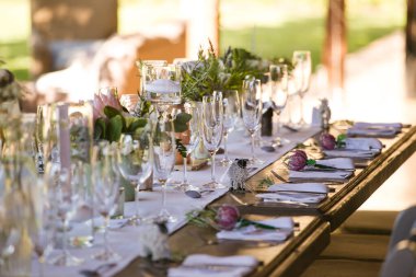 Bu büyüleyici görüntü, gerçek bir düğünün zarif dekorunu ve büyüleyici çiçek düzenlemelerini gözler önüne seriyor. Fotoğrafta zarif çiçekler, mumlar ve diğer dekoratif el ile süslenmiş büyüleyici bir düğün yerinde güzel dekore edilmiş bir masa yer alıyor.