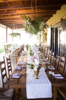 Bu büyüleyici görüntü, gerçek bir düğünün zarif dekorunu ve büyüleyici çiçek düzenlemelerini gözler önüne seriyor. Fotoğrafta zarif çiçekler, mumlar ve diğer dekoratif el ile süslenmiş büyüleyici bir düğün yerinde güzel dekore edilmiş bir masa yer alıyor.