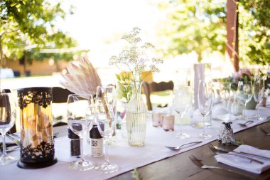 Bu büyüleyici görüntü, gerçek bir düğünün zarif dekorunu ve büyüleyici çiçek düzenlemelerini gözler önüne seriyor. Fotoğrafta zarif çiçekler, mumlar ve diğer dekoratif el ile süslenmiş büyüleyici bir düğün yerinde güzel dekore edilmiş bir masa yer alıyor.