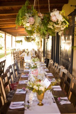 Bu büyüleyici görüntü, gerçek bir düğünün zarif dekorunu ve büyüleyici çiçek düzenlemelerini gözler önüne seriyor. Fotoğrafta zarif çiçekler, mumlar ve diğer dekoratif el ile süslenmiş büyüleyici bir düğün yerinde güzel dekore edilmiş bir masa yer alıyor.