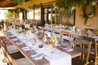 Bu büyüleyici görüntü, gerçek bir düğünün zarif dekorunu ve büyüleyici çiçek düzenlemelerini gözler önüne seriyor. Fotoğrafta zarif çiçekler, mumlar ve diğer dekoratif el ile süslenmiş büyüleyici bir düğün yerinde güzel dekore edilmiş bir masa yer alıyor.