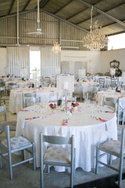 Bu büyüleyici görüntü, gerçek bir düğünün zarif dekorunu ve büyüleyici çiçek düzenlemelerini gözler önüne seriyor. Fotoğrafta zarif çiçekler, mumlar ve diğer dekoratif el ile süslenmiş büyüleyici bir düğün yerinde güzel dekore edilmiş bir masa yer alıyor.