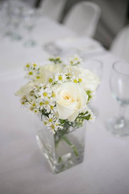 Bu büyüleyici görüntü, gerçek bir düğünün zarif dekorunu ve büyüleyici çiçek düzenlemelerini gözler önüne seriyor. Fotoğrafta zarif çiçekler, mumlar ve diğer dekoratif el ile süslenmiş büyüleyici bir düğün yerinde güzel dekore edilmiş bir masa yer alıyor.