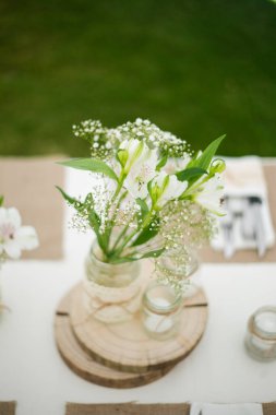 Bu büyüleyici görüntü, gerçek bir düğünün zarif dekorunu ve büyüleyici çiçek düzenlemelerini gözler önüne seriyor. Fotoğrafta zarif çiçekler, mumlar ve diğer dekoratif el ile süslenmiş büyüleyici bir düğün yerinde güzel dekore edilmiş bir masa yer alıyor.