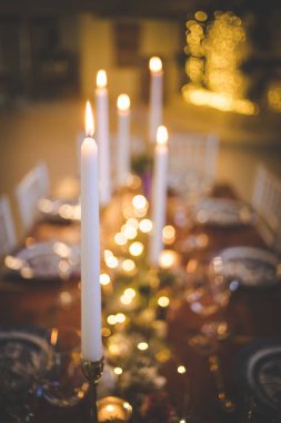 Bu büyüleyici görüntü, gerçek bir düğünün zarif dekorunu ve büyüleyici çiçek düzenlemelerini gözler önüne seriyor. Fotoğrafta zarif çiçekler, mumlar ve diğer dekoratif el ile süslenmiş büyüleyici bir düğün yerinde güzel dekore edilmiş bir masa yer alıyor.