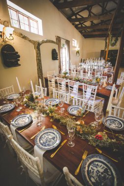 Bu büyüleyici görüntü, gerçek bir düğünün zarif dekorunu ve büyüleyici çiçek düzenlemelerini gözler önüne seriyor. Fotoğrafta zarif çiçekler, mumlar ve diğer dekoratif el ile süslenmiş büyüleyici bir düğün yerinde güzel dekore edilmiş bir masa yer alıyor.