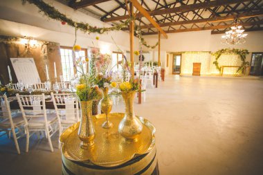 Bu büyüleyici görüntü, gerçek bir düğünün zarif dekorunu ve büyüleyici çiçek düzenlemelerini gözler önüne seriyor. Fotoğrafta zarif çiçekler, mumlar ve diğer dekoratif el ile süslenmiş büyüleyici bir düğün yerinde güzel dekore edilmiş bir masa yer alıyor.