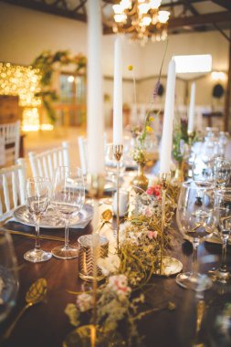 Bu büyüleyici görüntü, gerçek bir düğünün zarif dekorunu ve büyüleyici çiçek düzenlemelerini gözler önüne seriyor. Fotoğrafta zarif çiçekler, mumlar ve diğer dekoratif el ile süslenmiş büyüleyici bir düğün yerinde güzel dekore edilmiş bir masa yer alıyor.