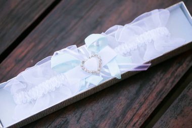 Bu büyüleyici görüntü, küpe, ayakkabı, jartiyer, mücevher ve parfüm gibi gelin aksesuarlarının yaratıcı ve sanatsal bir fotoğrafını sergiliyor. Fotoğraf çeşitli elementlerin güzel bir bileşimidir, karmaşık ayrıntıları vurgular. 