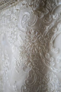 Bu büyüleyici görüntü, yaratıcı ve benzersiz bir şekilde fotoğraflanmış karmaşık detaylarla dolu bir gelinlik sergiliyor. Fotoğrafta karmaşık dantelli ve narin boncuklu çarpıcı beyaz bir gelinlik yer alıyor. Elbisenin fro fotografı var.