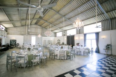 Bu büyüleyici görüntü, gerçek bir düğünün zarif dekorunu ve büyüleyici çiçek düzenlemelerini gözler önüne seriyor. Fotoğrafta zarif çiçekler, mumlar ve diğer dekoratif el ile süslenmiş büyüleyici bir düğün yerinde güzel dekore edilmiş bir masa yer alıyor.