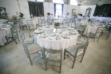 Bu büyüleyici görüntü, gerçek bir düğünün zarif dekorunu ve büyüleyici çiçek düzenlemelerini gözler önüne seriyor. Fotoğrafta zarif çiçekler, mumlar ve diğer dekoratif el ile süslenmiş büyüleyici bir düğün yerinde güzel dekore edilmiş bir masa yer alıyor.