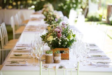 Bu büyüleyici görüntü, gerçek bir düğünün zarif dekorunu ve büyüleyici çiçek düzenlemelerini gözler önüne seriyor. Fotoğrafta zarif çiçekler, mumlar ve diğer dekoratif el ile süslenmiş büyüleyici bir düğün yerinde güzel dekore edilmiş bir masa yer alıyor.