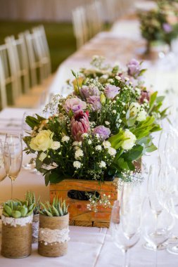 Bu büyüleyici görüntü, gerçek bir düğünün zarif dekorunu ve büyüleyici çiçek düzenlemelerini gözler önüne seriyor. Fotoğrafta zarif çiçekler, mumlar ve diğer dekoratif el ile süslenmiş büyüleyici bir düğün yerinde güzel dekore edilmiş bir masa yer alıyor.