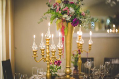 Bu büyüleyici görüntü, gerçek bir düğünün zarif dekorunu ve büyüleyici çiçek düzenlemelerini gözler önüne seriyor. Fotoğrafta zarif çiçekler, mumlar ve diğer dekoratif el ile süslenmiş büyüleyici bir düğün yerinde güzel dekore edilmiş bir masa yer alıyor.