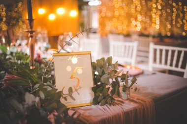 Bu büyüleyici görüntü, gerçek bir düğünün zarif dekorunu ve büyüleyici çiçek düzenlemelerini gözler önüne seriyor. Fotoğrafta zarif çiçekler, mumlar ve diğer dekoratif el ile süslenmiş büyüleyici bir düğün yerinde güzel dekore edilmiş bir masa yer alıyor.