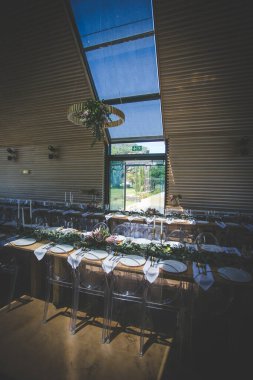 Bu büyüleyici görüntü, gerçek bir düğünün zarif dekorunu ve büyüleyici çiçek düzenlemelerini gözler önüne seriyor. Fotoğrafta zarif çiçekler, mumlar ve diğer dekoratif el ile süslenmiş büyüleyici bir düğün yerinde güzel dekore edilmiş bir masa yer alıyor.