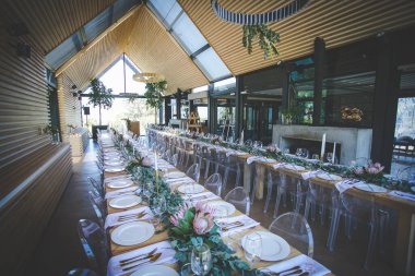 Bu büyüleyici görüntü, gerçek bir düğünün zarif dekorunu ve büyüleyici çiçek düzenlemelerini gözler önüne seriyor. Fotoğrafta zarif çiçekler, mumlar ve diğer dekoratif el ile süslenmiş büyüleyici bir düğün yerinde güzel dekore edilmiş bir masa yer alıyor.