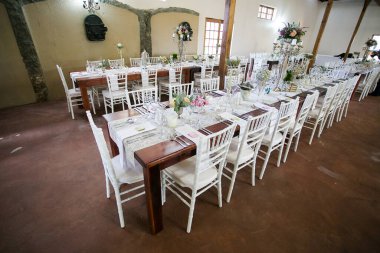 Bu büyüleyici görüntü, gerçek bir düğünün zarif dekorunu ve büyüleyici çiçek düzenlemelerini gözler önüne seriyor. Fotoğrafta zarif çiçekler, mumlar ve diğer dekoratif el ile süslenmiş büyüleyici bir düğün yerinde güzel dekore edilmiş bir masa yer alıyor.