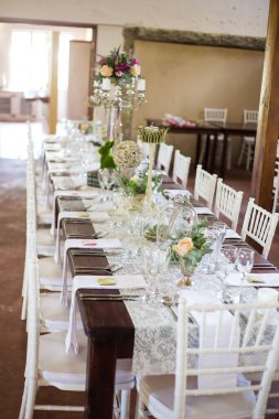 Bu büyüleyici görüntü, gerçek bir düğünün zarif dekorunu ve büyüleyici çiçek düzenlemelerini gözler önüne seriyor. Fotoğrafta zarif çiçekler, mumlar ve diğer dekoratif el ile süslenmiş büyüleyici bir düğün yerinde güzel dekore edilmiş bir masa yer alıyor.