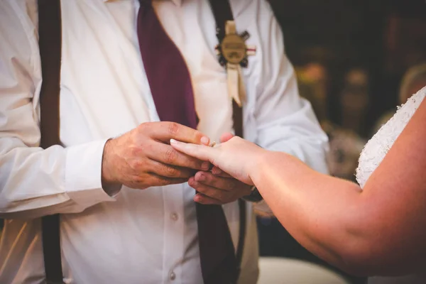 This beautiful image captures the intimate moment of a couple exchanging wedding rings at a real wedding. The photograph features a close-up of the couple\'s hands, showcasing their intertwined fingers and the wedding bands on their fingers. The image
