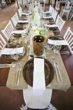 Bu büyüleyici görüntü, gerçek bir düğünün zarif dekorunu ve büyüleyici çiçek düzenlemelerini gözler önüne seriyor. Fotoğrafta zarif çiçekler, mumlar ve diğer dekoratif el ile süslenmiş büyüleyici bir düğün yerinde güzel dekore edilmiş bir masa yer alıyor.