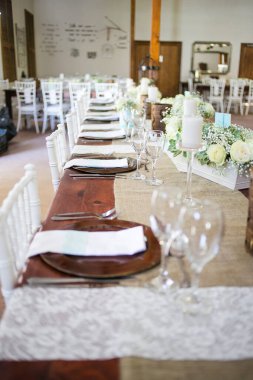 Bu büyüleyici görüntü, gerçek bir düğünün zarif dekorunu ve büyüleyici çiçek düzenlemelerini gözler önüne seriyor. Fotoğrafta zarif çiçekler, mumlar ve diğer dekoratif el ile süslenmiş büyüleyici bir düğün yerinde güzel dekore edilmiş bir masa yer alıyor.